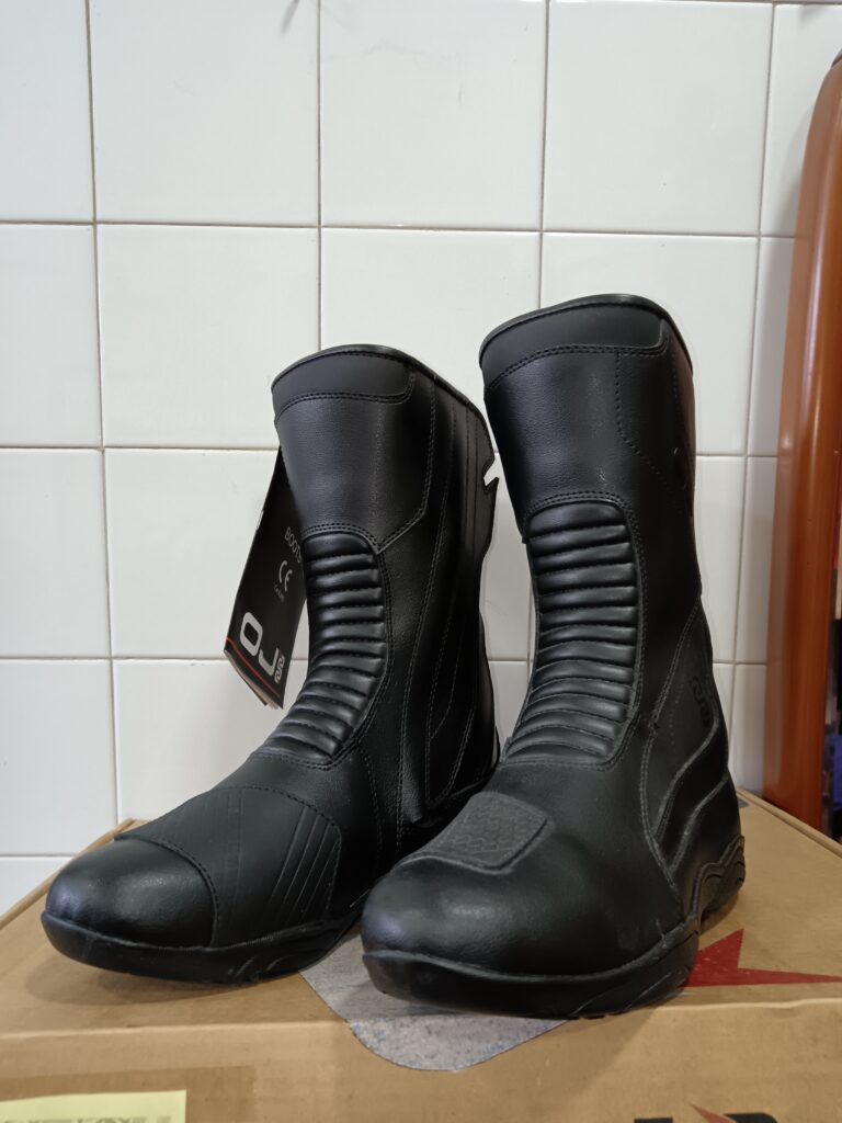 Botas de moto OJ Massive negras, talla 39, de caña alta, con pliegues tipo acordeón y protectores, sobre caja de cartón.