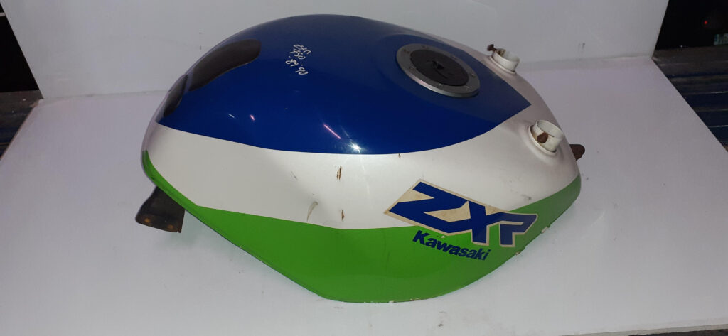 Vista lateral de un depósito de gasolina original usado para Kawasaki ZXR 750 (modelos 1988-1989), con decoración tri-color blanca, azul y verde. Se observa el logo adhesivo "ZXR Kawasaki" en el lateral, tapón de llenado central, un protector texturizado y una marca manuscrita "ZXR 750 88/89". Pieza para restauración.