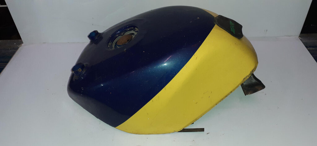 Depósito de gasolina original para Kawasaki ZXR con decoración clásica azul y amarilla. Vista lateral mostrando el diseño geométrico, el protector central con el logo ZXR en verde y los soportes de fijación.