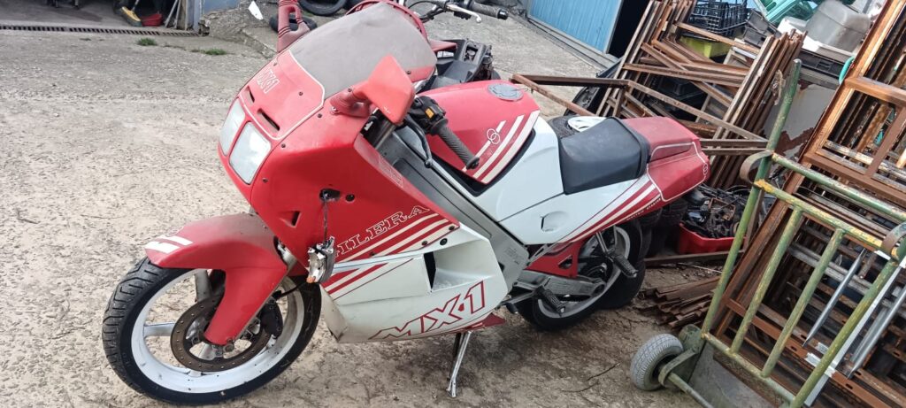 Vista lateral de una motocicleta Gilera MX1 roja y blanca destinada a despiece, mostrando carenado frontal, depósito y parte ciclo sobre suelo de hormigón.