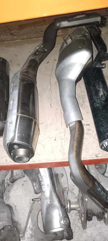 Dos silenciadores de escape originales para Honda CBR 600 RR (modelos 2003 a 2005) sobre estante de taller. Se aprecia el acabado metálico original y los colectores de conexión en perfecto estado de conservación para recambio.