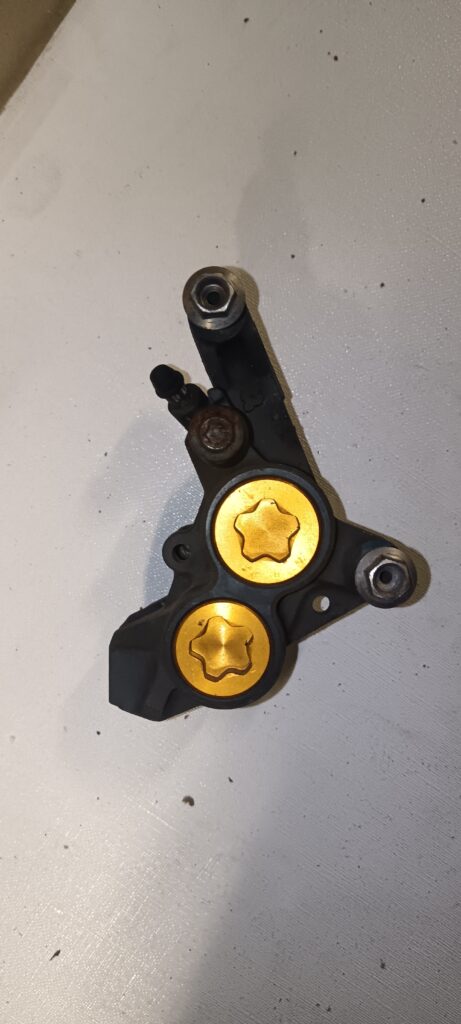 Pinza de freno delantera radial original para Yamaha R6 y R1, con acabado en negro y tapones dorados de pistones. Recambio de alto rendimiento.