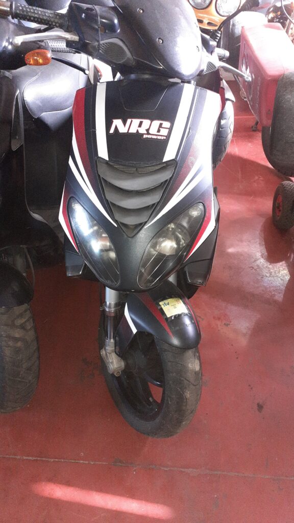 Vista frontal de scooter Gilera NRG Power 50cc usada para despiece en taller. Se aprecian el escudo frontal con faros dobles, manillar con intermitente, guardabarros delantero y rueda. Recambios y piezas a consultar en Vayafaba.