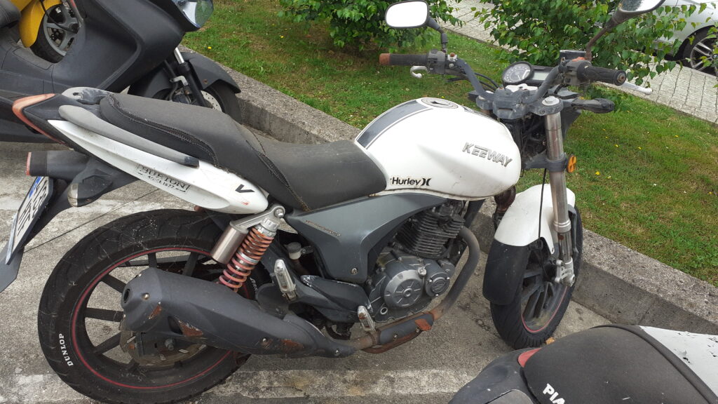 Vista lateral derecha de moto Keeway RKV 125 blanca usada para despiece. Se aprecian el depósito con pegatinas, asiento, motor monocilíndrico, escape y llantas de aleación. Recambios y piezas a consultar en Vayafaba.