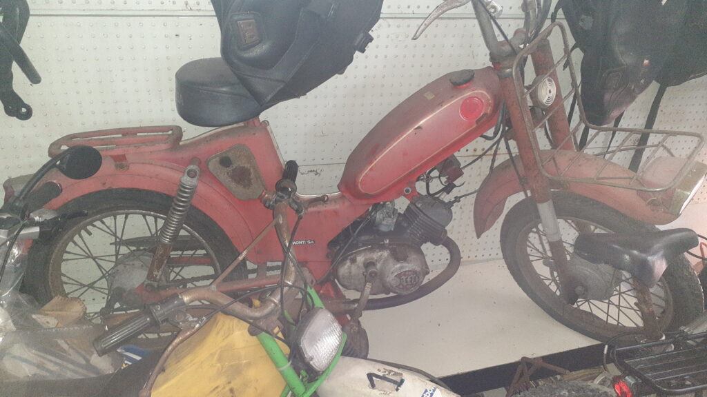 Mini Montesa 50 cc de 1968 color rojo para restauración completa. Vista lateral derecha de la motocicleta clásica de desguace con óxido y polvo. Motor 50cc de época, depósito original y chasis visibles en el taller de Vayafaba.