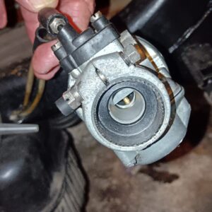 Vista lateral de carburador DellOrto SHA 12-12 para Vespino, mostrando la entrada de aire circular y tornillo de ajuste.