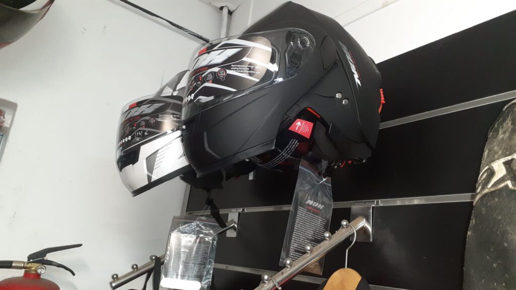 Cascos de moto abatibles NOX en negro mate y blanco brillante. Exposición en tienda con visores solares integrados.