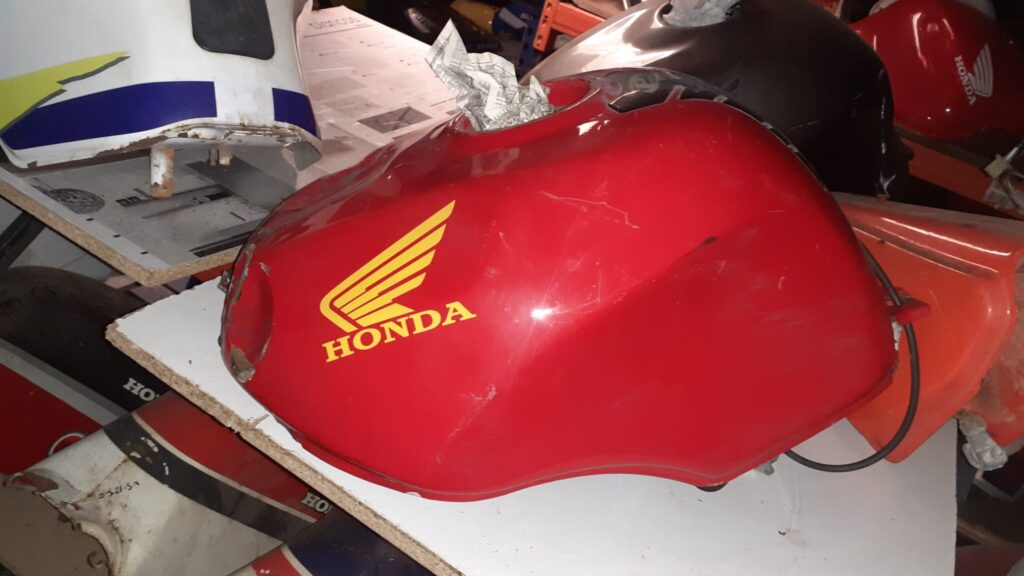 Depósito de gasolina rojo original para Honda CBR 900 RR de 1992 en un estante de desguace.
