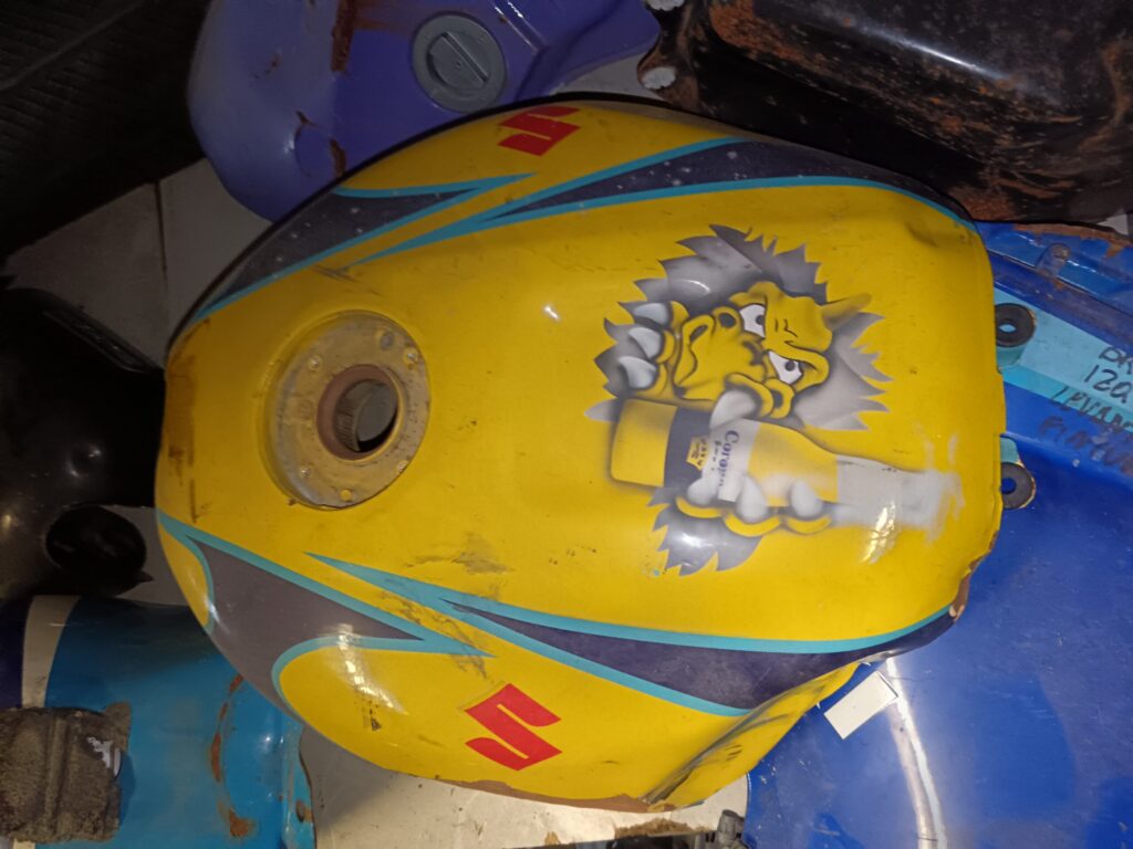 Depósito usado Suzuki GSX-R 750 (2000), color amarillo con gráfico Corona Extra, sin tapón, con abolladura lateral.