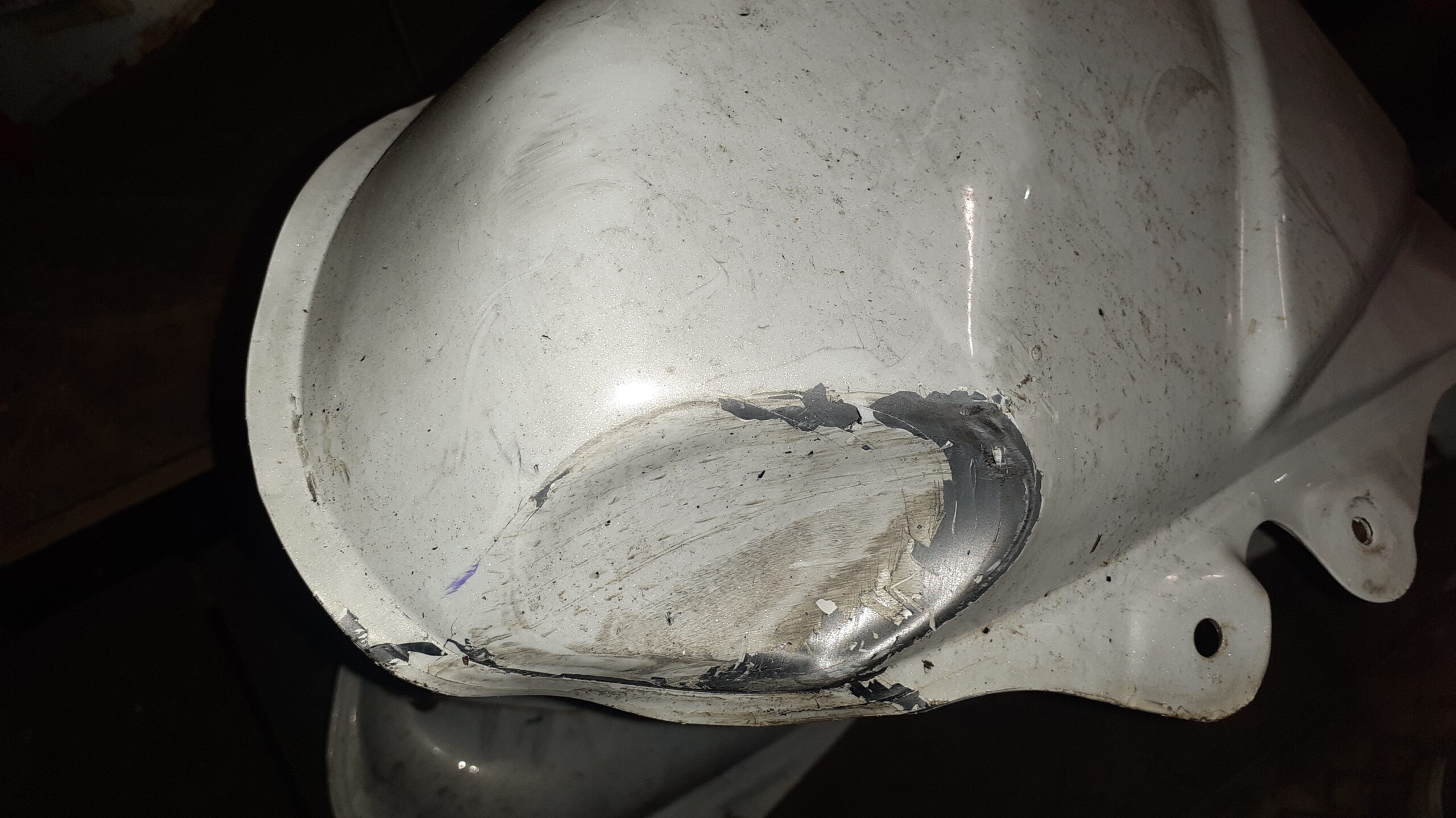 Primer plano de abolladura en lateral de depósito Suzuki V-Strom 650 2011 blanco. El metal no presenta grietas ni fugas.