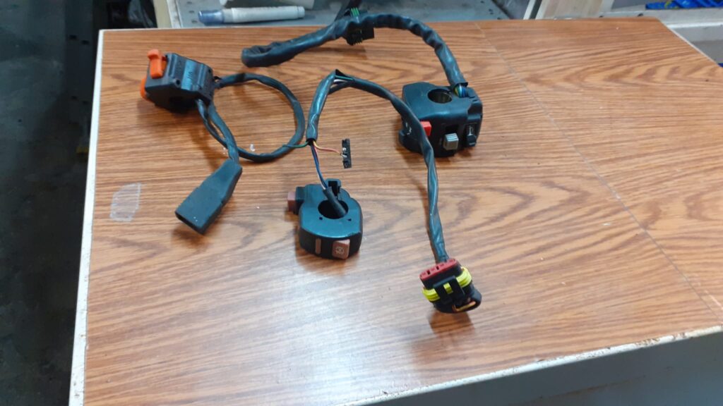 Conjunto de conmutadores de luces y mandos de manillar usados para moto. Varias unidades con cableado y conectores visibles.