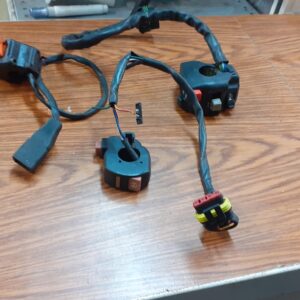 Conjunto de conmutadores de luces y mandos de manillar usados para moto. Varias unidades con cableado y conectores visibles.