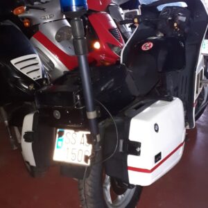 Vista trasera de moto BMW K75 de 1992 blanca estilo patrulla con maletas rígidas, mástil de sirena azul y matrícula.