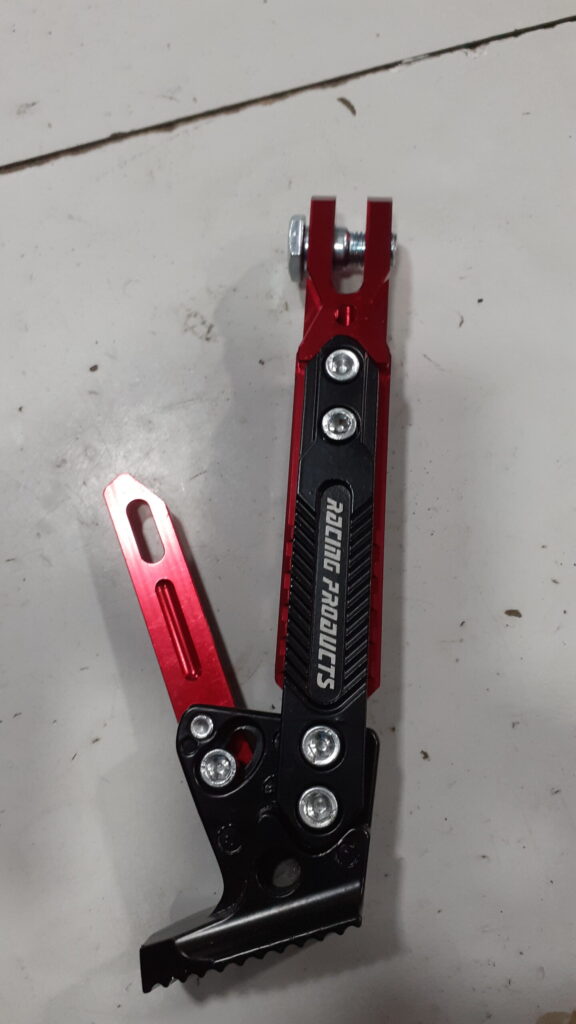 Vista lateral de la pata de cabra universal ajustable de aluminio rojo y negro para moto, destacando su diseño ergonómico.