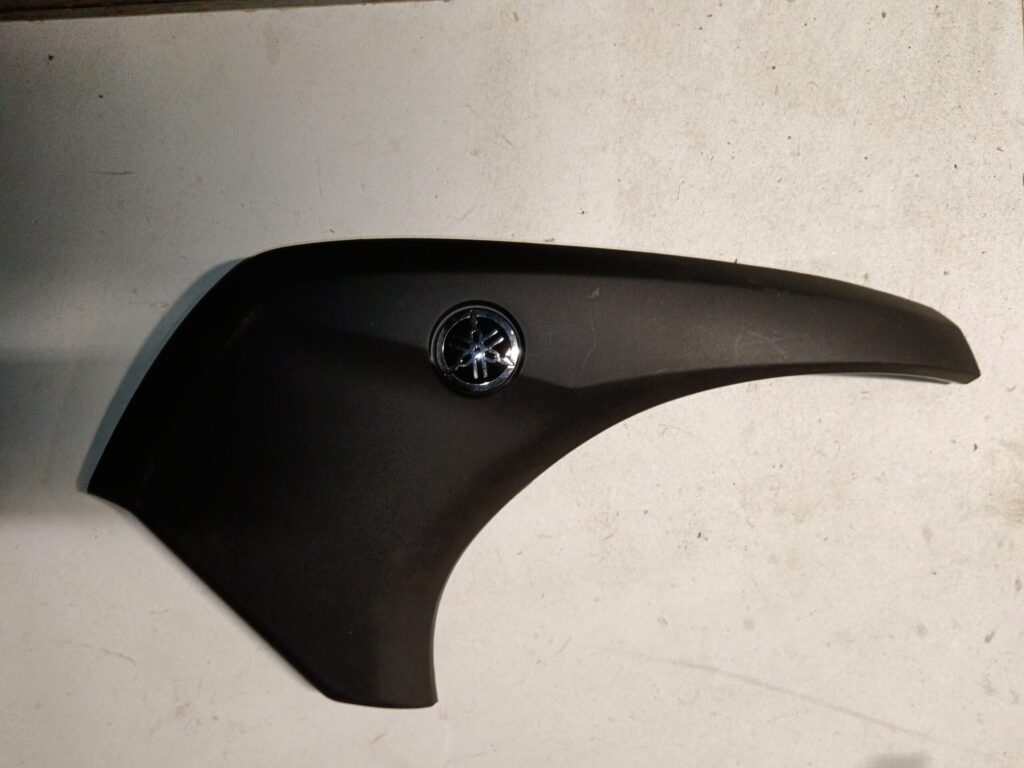 Tapa lateral delantera derecha original para scooter Yamaha Tricity 125. Color negro mate con emblema cromado Yamaha.
