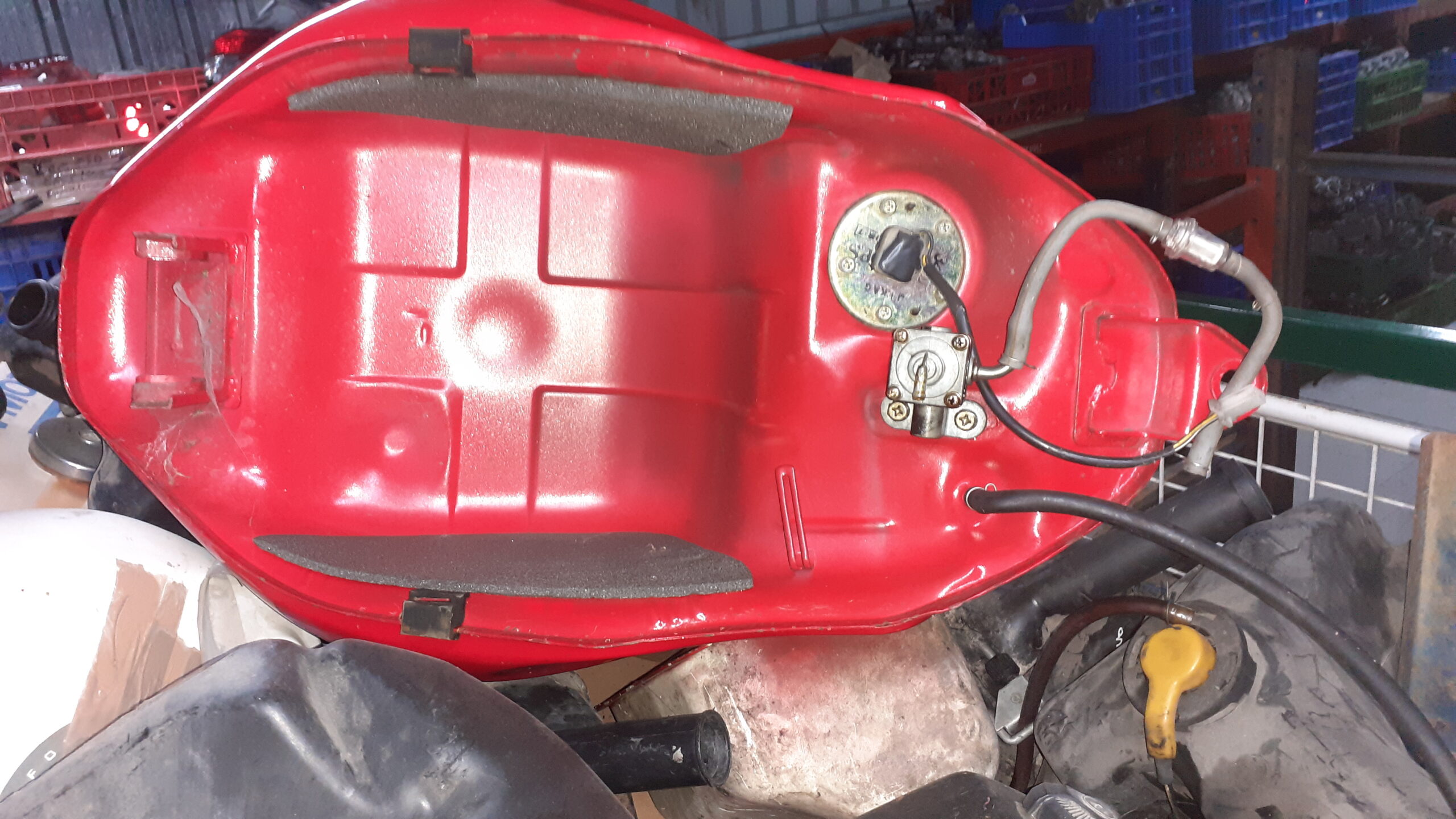 Vista inferior del depósito Hyosung GTR 125 rojo. Detalle del grifo de gasolina, bomba y anclajes del chasis originales.
