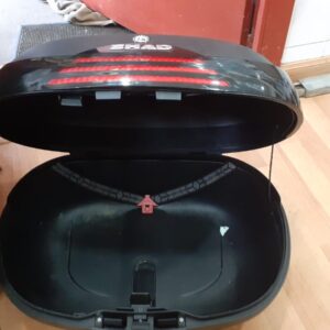 Baúl Shad abierto para moto, negro con reflectante rojo, mostrando el interior espacioso con correas de sujeción técnicas.