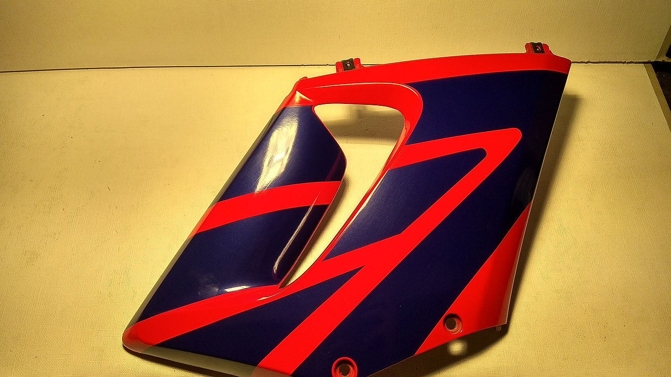Vista exterior del carenado lateral derecho original en color azul y rojo con soportes superiores metálicos para motocicleta Honda CBR 125 R.