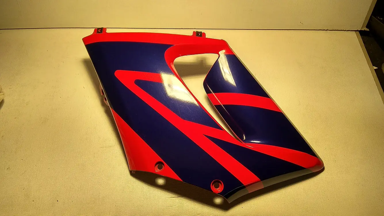 Vista exterior del carenado lateral izquierdo original en colores azul y rojo con soportes intactos para motocicleta Honda CBR 125 R.