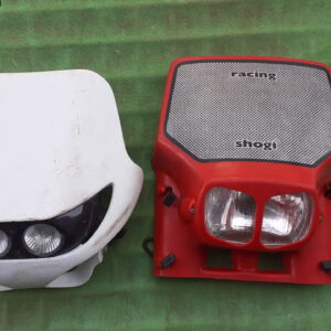 Pareja de caretas de faro universales homologadas para moto de enduro, modelos Acerbis blanco y Shogi rojo.