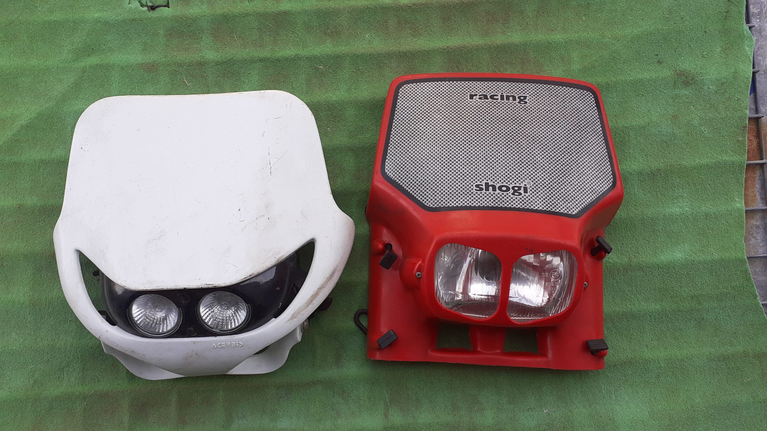 Pareja de caretas de faro universales homologadas para moto de enduro, modelos Acerbis blanco y Shogi rojo.