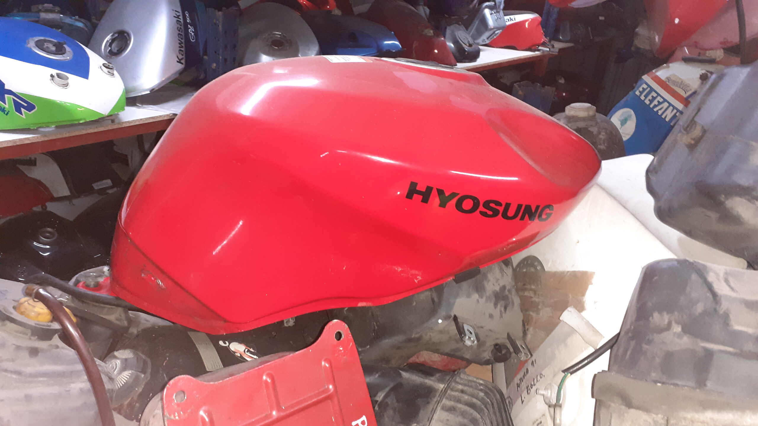 Depósito de combustible rojo para moto Hyosung GTR 125. Recambio original de despiece con logotipos de marca visibles.
