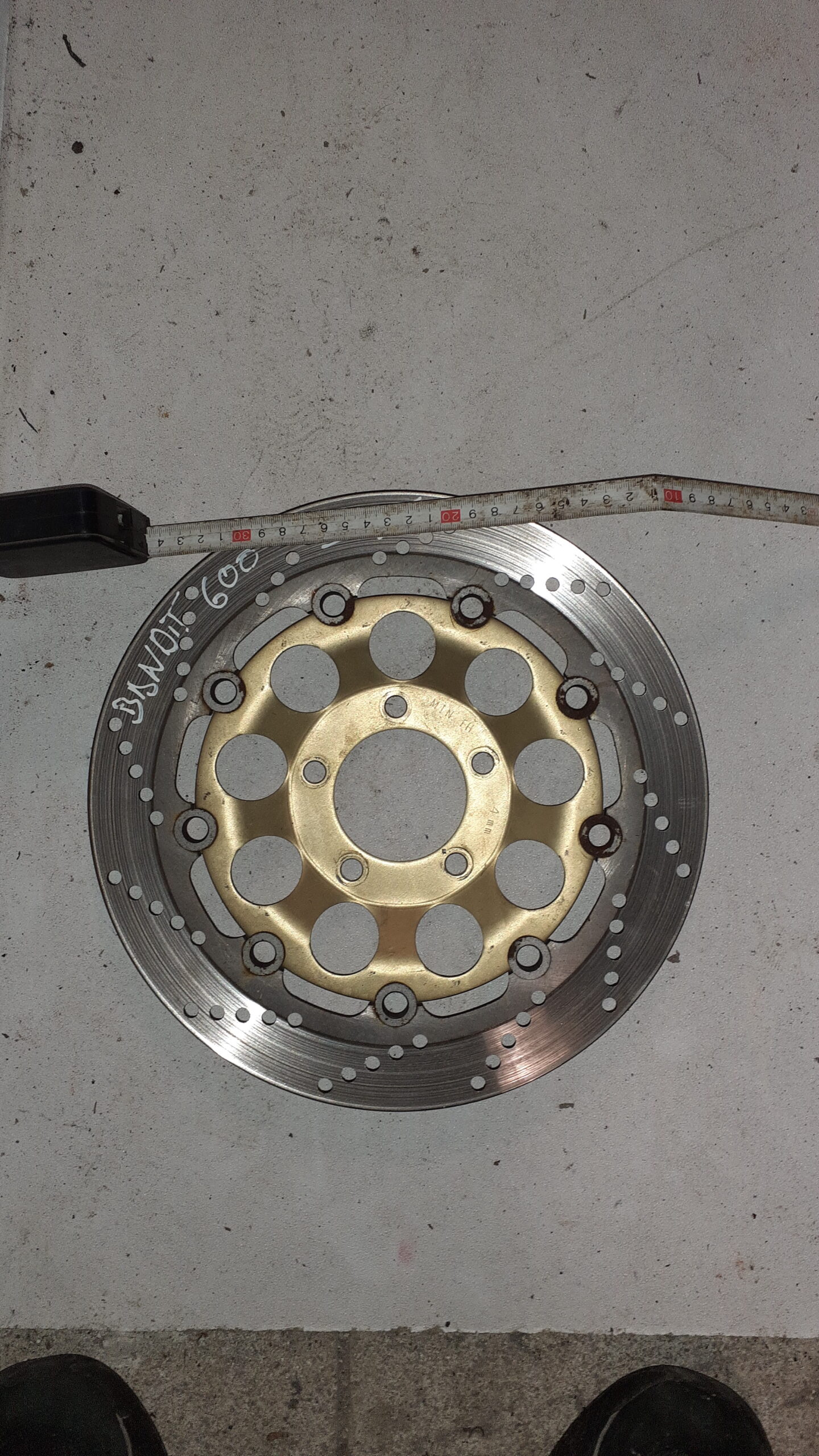 Medición de un disco de freno delantero de Suzuki Bandit 600 año 2004, con núcleo dorado y cinta métrica sobre el borde.