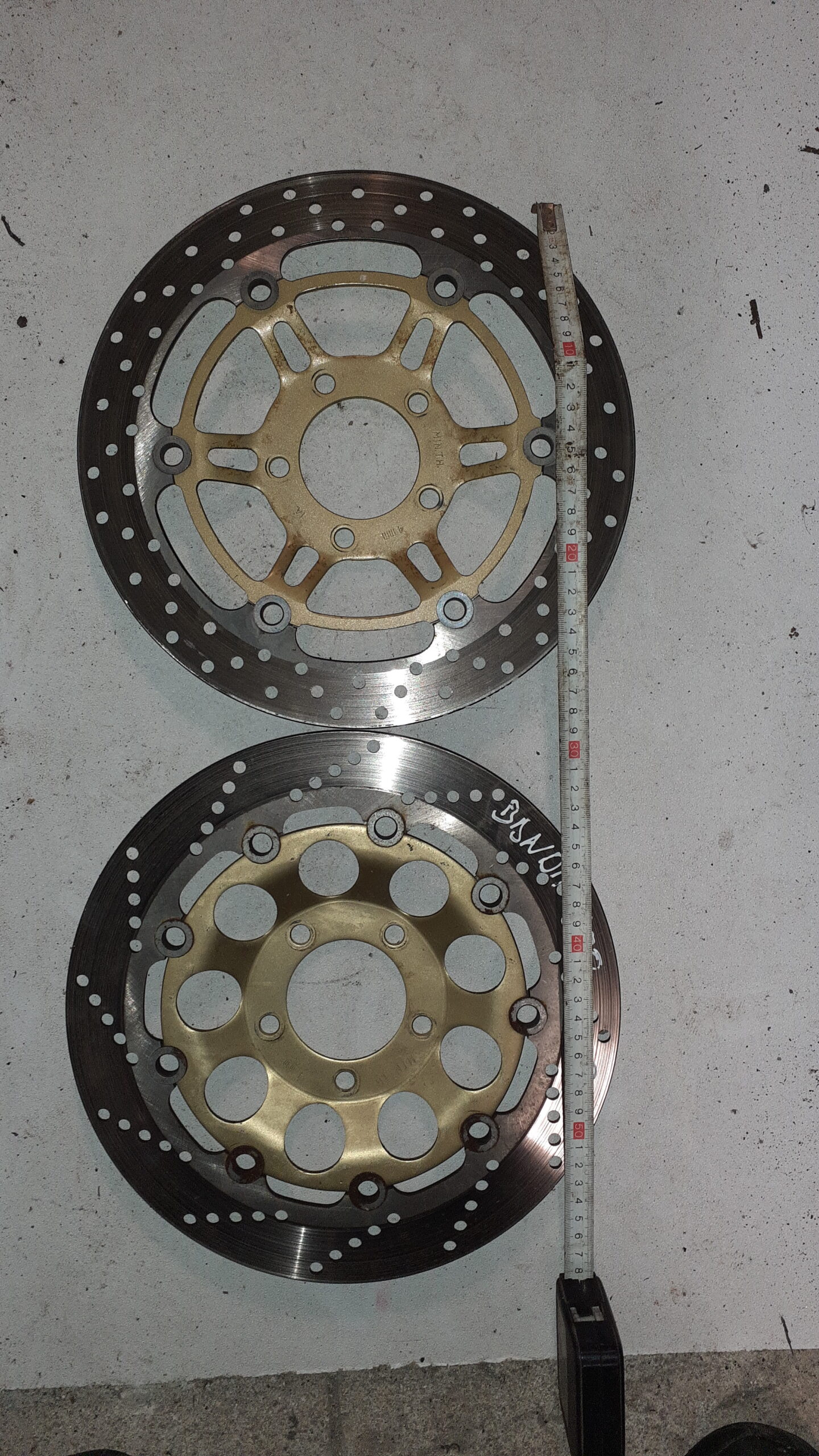 Dos discos de freno delanteros para Suzuki Bandit 600 año 2004, con núcleos dorados y cinta métrica sobre fondo de cemento.