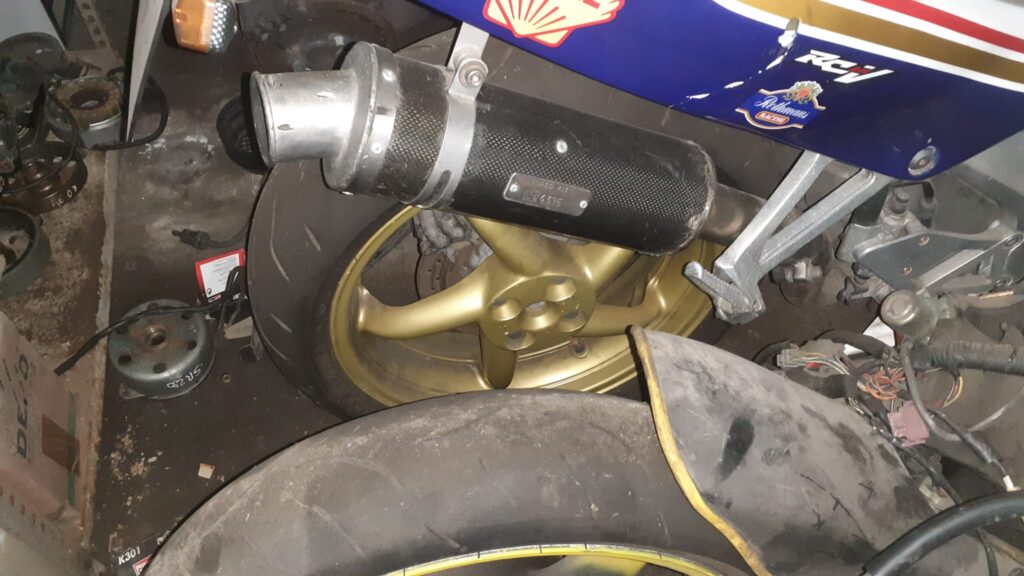 Tubo de escape de carbono homologado montado en una Honda VFR 750 de 1992, mostrando la chapa de homologación y la llanta.