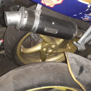 Tubo de escape de carbono homologado montado en una Honda VFR 750 de 1992, mostrando la chapa de homologación y la llanta.