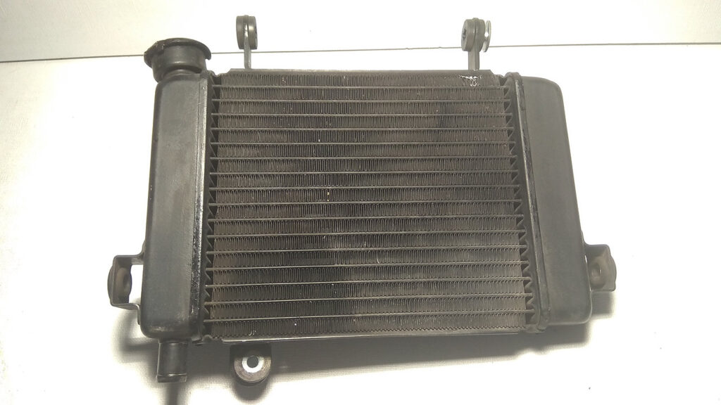 Vista frontal del radiador de agua de aluminio original en color negro para motocicleta Honda CBR 125 R años 2004 a 2006.