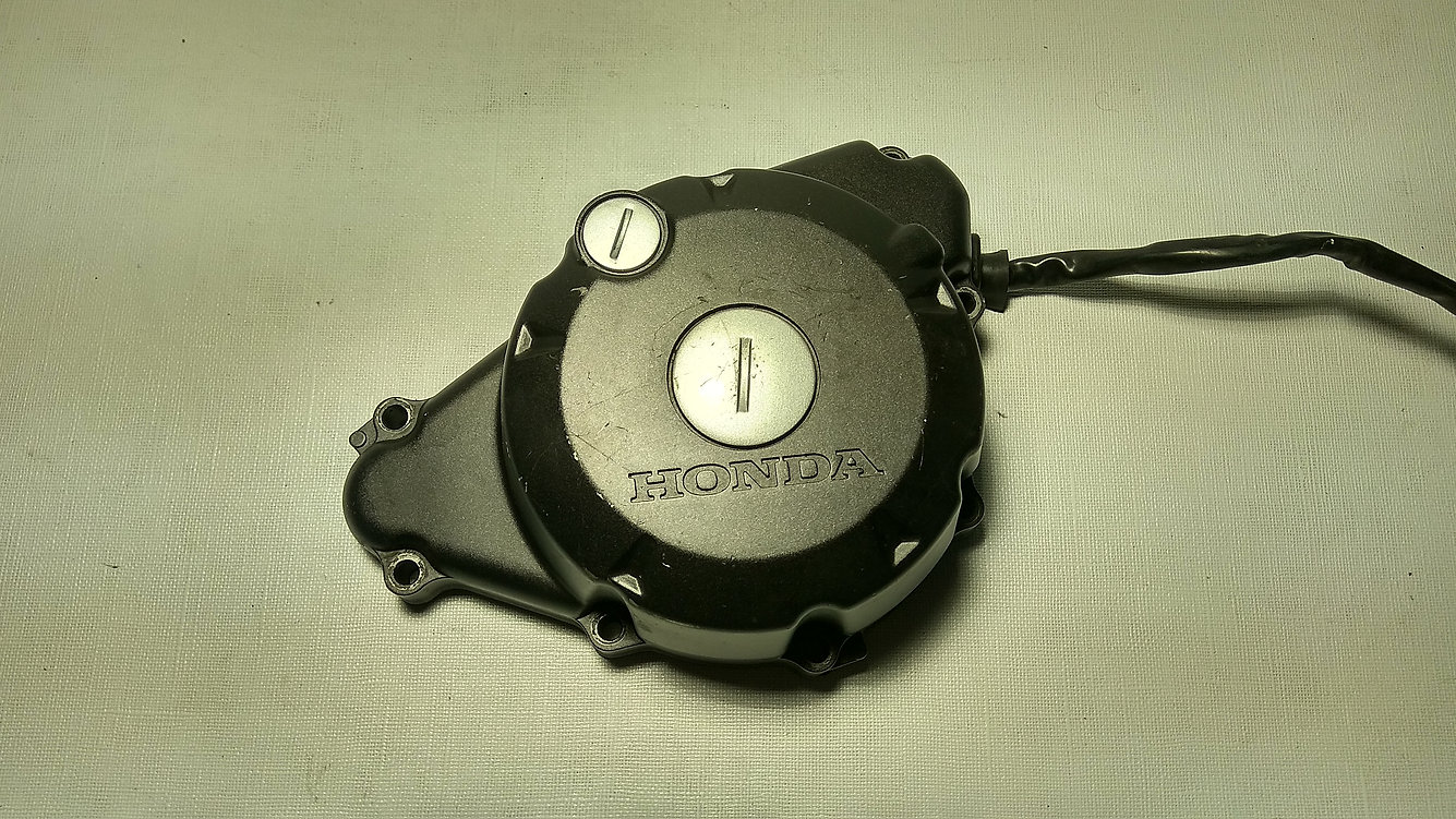 Vista exterior de la tapa de alternador y cárter de encendido original negra con logotipo grabado para motocicleta Honda CBR 125 R años 2004 a 2006.