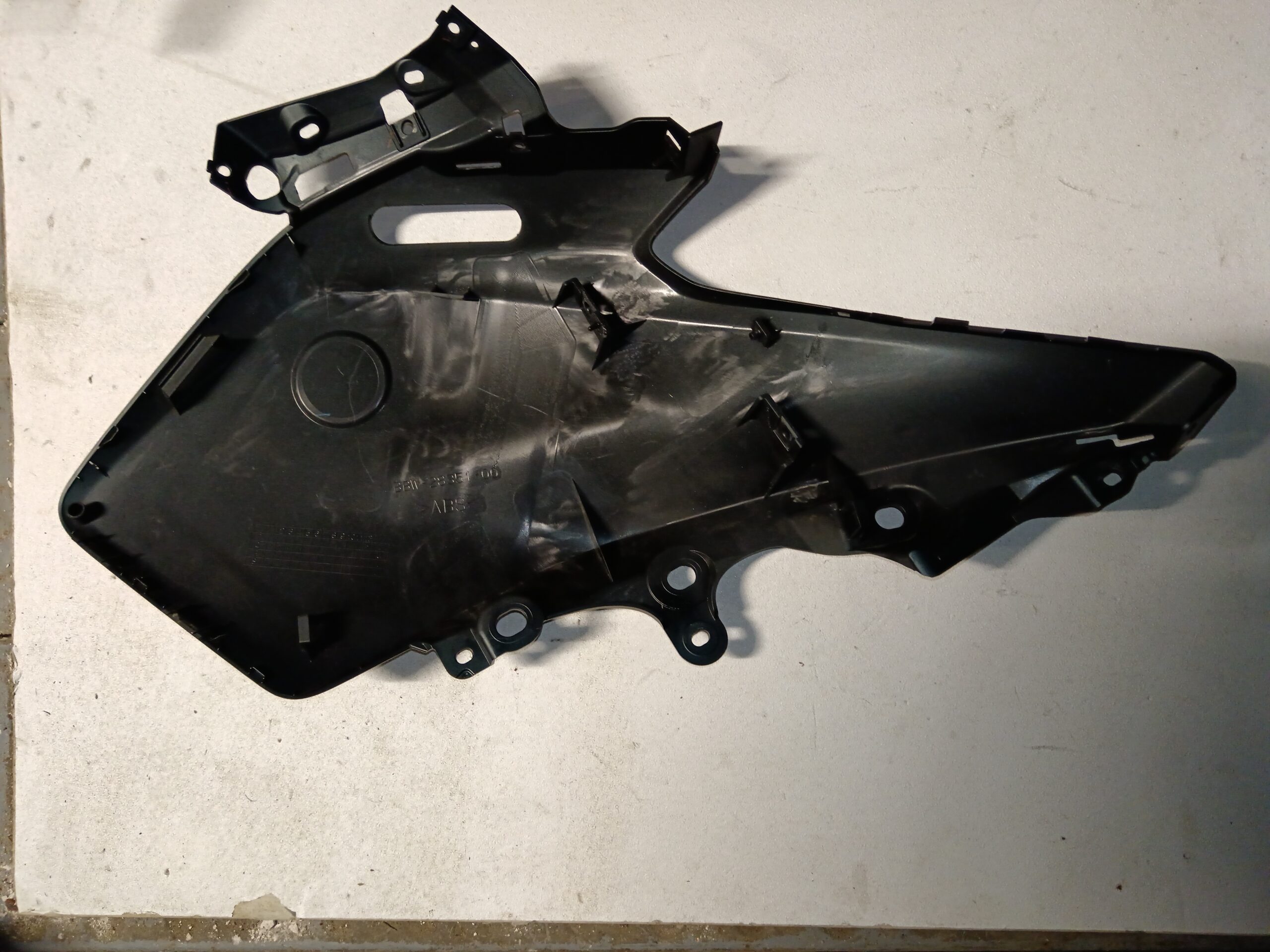 Vista interior de la tapa lateral izquierda para Yamaha XMAX 125, mostrando puntos de anclaje y clips de sujeción originales.